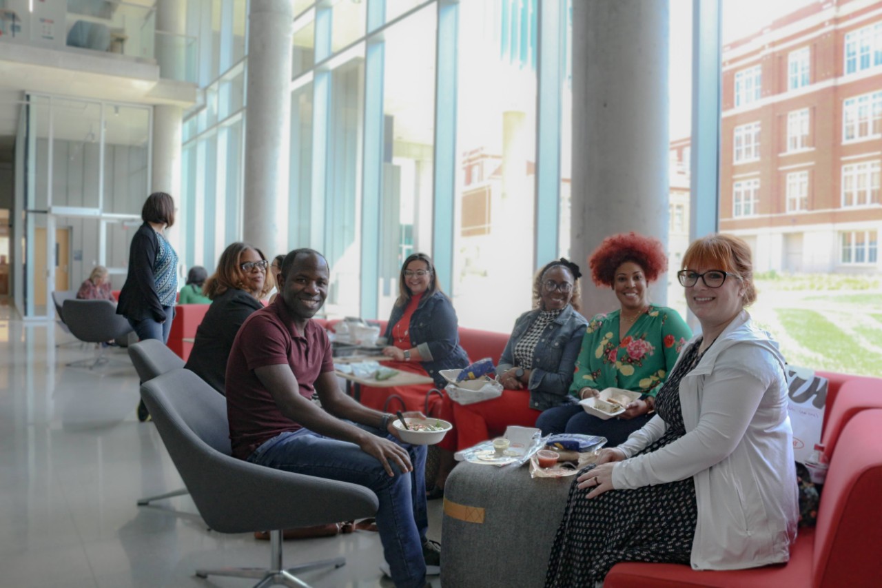 Faculty sit inside the HSB and smile at the camera.
